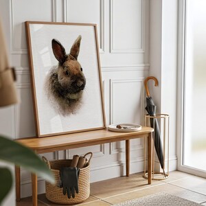 May include: A rectangular framed wall art print featuring a detailed portrait of a brown and grey rabbit. The artwork is displayed in a light wood frame, showcasing the animal's fur texture and long ears against a plain white background.