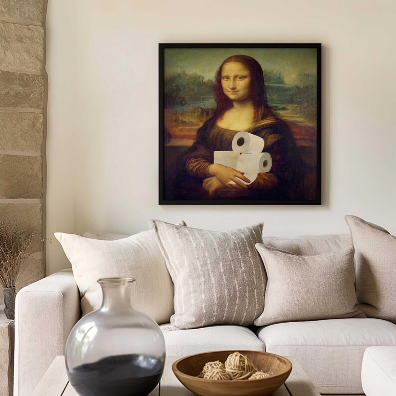 K&ouml;nnte beinhalten: Ein gerahmter Druck der Mona Lisa, die Toilettenpapierrollen h&auml;lt. Das Kunstwerk wird &uuml;ber einem wei&szlig;en Sofa mit beigen Kissen gezeigt. Eine Glasvase und eine Holzschale befinden sich im Vordergrund.
