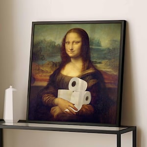 K&ouml;nnte beinhalten: Gerahmter Druck der Mona Lisa, die drei Rollen Toilettenpapier h&auml;lt. Das Kunstwerk ist eine Parodie des urspr&uuml;nglichen Renaissance-Gem&auml;ldes, mit einem schwarzen Rahmen und einem neutralen Hintergrund.