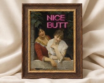 May include: A dark brown wooden frame with gold trim containing a print of two people leaning on a stone ledge. The print features the neon pink text NICE BUTT overlaid on the scene. The people are wearing red and white clothing.