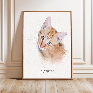 May include: A framed portrait print featuring a watercolor-style illustration of an orange tabby kitten looking upward. The kitten has light green eyes and a pink nose. Below the kitten, the name Cooper is written in a black cursive script.