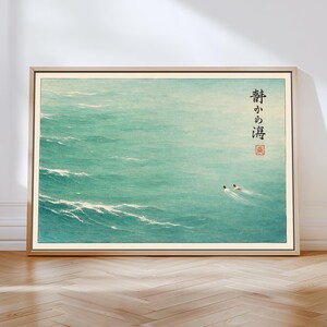 May include: Framed art print featuring a serene ocean scene in shades of teal and white. Two figures are swimming in the water. Japanese text is printed vertically on the right side of the artwork. The artwork is in a light-colored wooden frame.