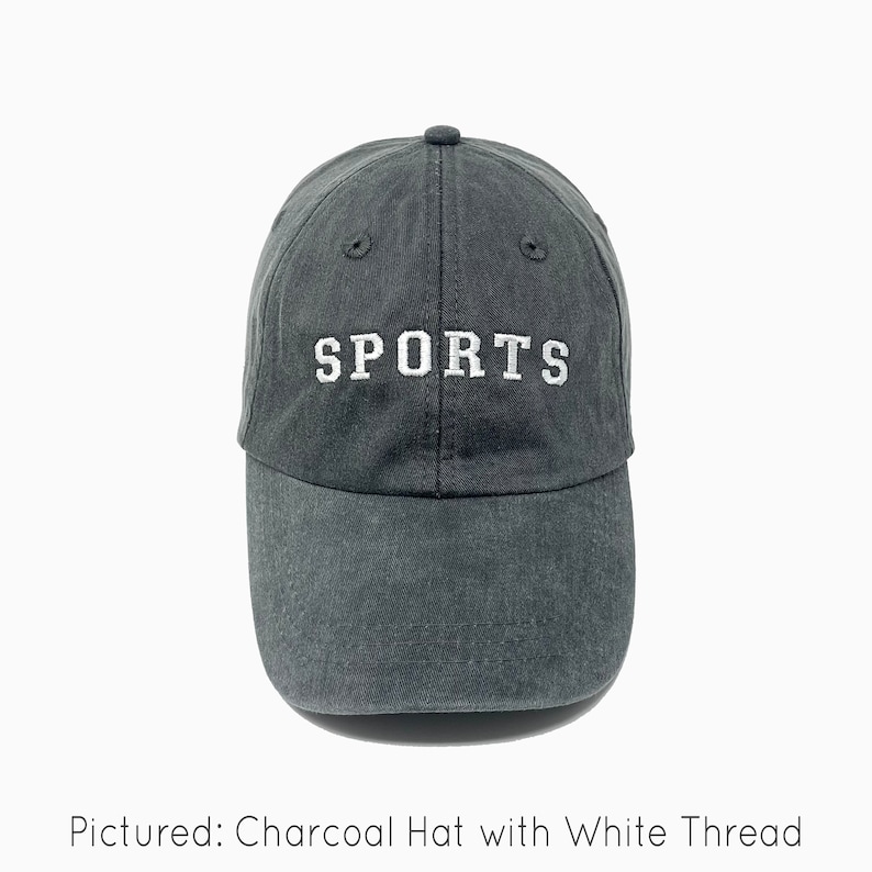 A charcoal gray baseball cap is shown with embroidered text saying "sports" in all uppercase in an athletic type font with white thread. The baseball cap is pigment-dyed and features a faded/worn in look due to this.