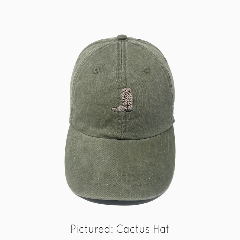 A cactus green baseball cap is shown with an embroidered cowboy boot. The boot is light tan with dark brown accents and a dark gray sole. The baseball cap is pigment-dyed and features a faded/worn in look due to this.