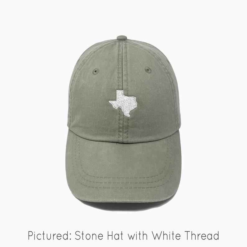 A stone/tan baseball cap is shown with embroidered image of the state of Texas in white thread. The baseball cap is pigment-dyed and features a faded/worn in look due to this.