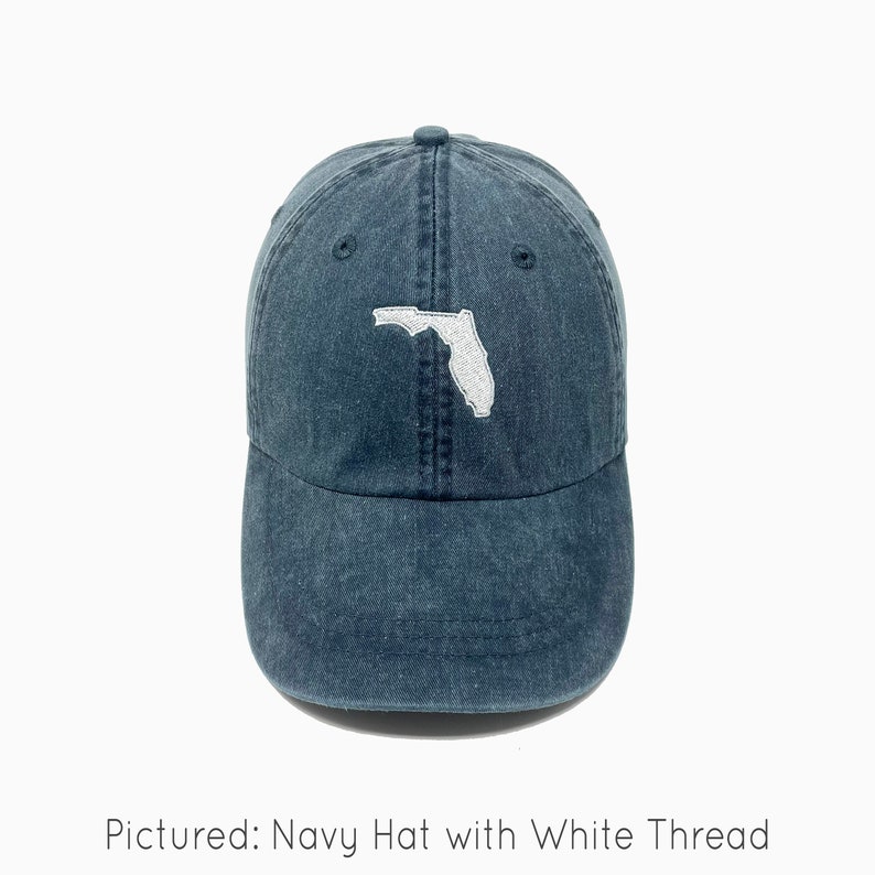 A navy baseball cap is shown with an embroidered image of the state of Florida in white thread. The baseball cap is pigment-dyed and features a faded/worn in look due to this.