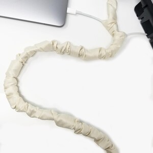 Może przedstawiać: Biały organizer kablowy z tkaniny owinięty wokół białego kabla. Kabel jest podłączony do laptopa i urządzenia.