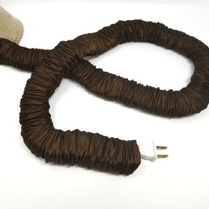 May include: A brown fabric cord cover with a white electrical plug. The cord is coiled and ready to be used.