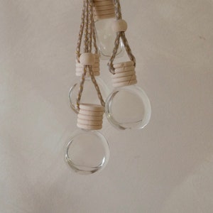 May include: Three glass bottles with wooden stoppers and beige string hanging from a beige string with gold accents.