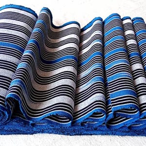 May include: Rolled and folded blue, white, and black striped fabric. The fabric has a blue border and is arranged to show the pattern. The stripes are wavy and create a textured appearance. The fabric is likely used for textiles or home decor.