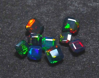 Puede incluir: Colección de piedras preciosas de ópalo negro facetadas. Los ópalos muestran una gama de colores, incluyendo verde, azul, rojo y naranja, sobre un fondo oscuro. Las piedras están talladas en formas cuadradas o rectangulares.