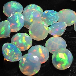 May include: A collection of 14 iridescent opal gemstones, each with a unique pattern of color and light. The opals are faceted and have a round shape.
