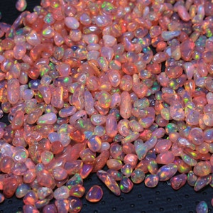 May include: A large pile of small, iridescent pink opal stones. The stones are smooth and have a variety of shapes and sizes.