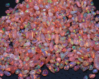 May include: A large pile of small, iridescent pink opal stones. The stones are smooth and have a variety of shapes and sizes.