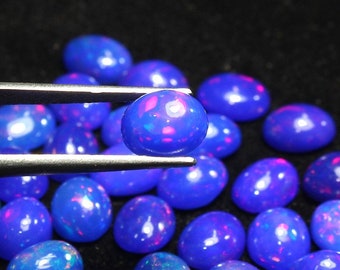May include: A collection of oval-shaped blue opal gemstones with iridescent flashes of color. The stones are arranged in a loose pile, with one stone being held by tweezers.