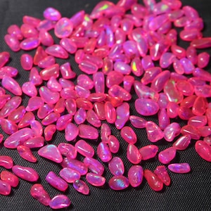 May include: A large pile of pink opal gemstone chips. The chips are iridescent and have a variety of shapes and sizes.