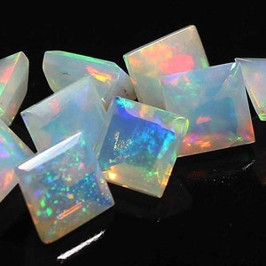 Puede incluir: Un grupo de ocho piedras preciosas de ópalo blanco iridiscente, cortadas en forma cuadrada, con una variedad de colores arcoíris que se reflejan en la superficie.