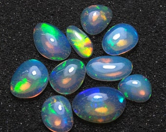 May include: A collection of ten oval-shaped opals with iridescent colors, including green, blue, and orange. The opals are arranged on a black surface.
