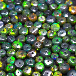 May include: A close-up of a collection of dark green, black, and iridescent opal beads. The beads are faceted and have a hole drilled through the center. The beads are arranged in a random pattern.