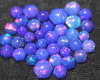 May include: A collection of blue opal gemstones with iridescent flashes of pink, green, and yellow. The opals are various sizes and shapes, including round and faceted, and are arranged on a dark surface. These gemstones are suitable for jewelry making.