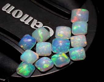 May include: A collection of iridescent opal gemstones. The opals are square or cushion-cut, displaying a play of color with flashes of blue, green, and red. The gemstones are arranged on a black surface.