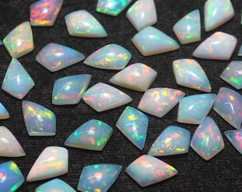 May include: A collection of iridescent opal gemstones in various shapes, including triangles and trapezoids. The opals display a play of color with flashes of blue, green, yellow, and red. The gemstones are scattered on a dark surface.