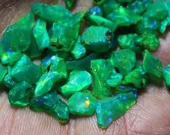 May include: A collection of green opal gemstones, with some showing iridescent flashes of color. The opals are rough and have an irregular shape.