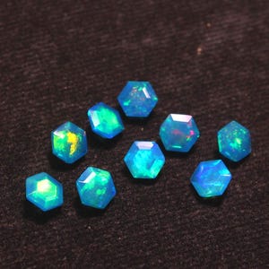 May include: A collection of faceted, hexagonal opals. The opals display a vibrant play of color, with flashes of blue, green, and yellow. The gemstones are set against a dark, textured background, highlighting their brilliance.