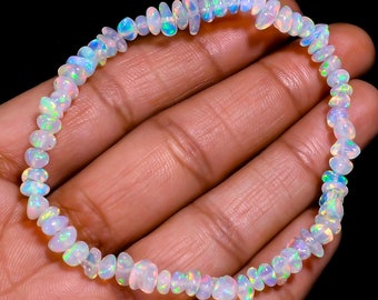 Könnte beinhalten: Ein Armband aus weißem Opal mit schillernden Regenbogenfarben. Das Armband besteht aus kleinen, unregelmäßig geformten Perlen.