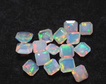 May include: A collection of faceted opal gemstones with a square or rectangular shape. The opals display a play of color, with flashes of green, blue, and orange hues. The gemstones are set against a dark background.