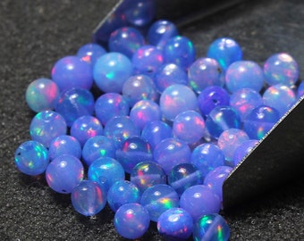 May include: A close-up of a pile of iridescent blue opal beads. The beads are round and have a smooth, polished finish. They are scattered on a dark gray surface.