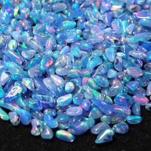 May include: A collection of polished opals, predominantly light blue with iridescent colours. The gemstones are oval-shaped and vary in size. The opals have a smooth, glossy surface with flashes of pink, green, and yellow. The background is black.