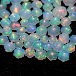 Peut inclure: Une collection d'opales iridescentes taillées en forme hexagonale. Les opales présentent une gamme de couleurs, notamment le bleu, le vert et des éclats de rouge et de jaune. Les pierres précieuses sont disposées de près, créant un effet chatoyant sur fond sombre.