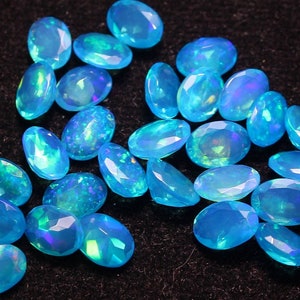 Könnte beinhalten: Eine Sammlung ovaler blauer Opal-Edelsteine mit schillernden Farbflecken. Die Steine sind in einem zufälligen Muster auf einer schwarzen Oberfläche angeordnet.