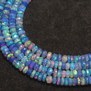 May include: Close-up of several strands of faceted blue opal beads. The beads have a vibrant, iridescent quality, with flashes of green, pink, and yellow. The beads are strung together, creating a necklace or bracelet.