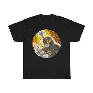 Könnte beinhalten: Schwarzes T-Shirt mit einem kreisförmigen Grafikdruck eines Käferwesens mit großen Hörnern und leuchtend gelben Augen. Das Wesen hält eine große, silberne Waffe. Der Hintergrund des Grafikdrucks ist ein gelbes und oranges abstraktes Design.