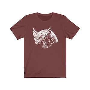 May include: A maroon t-shirt with a white graphic print of a stylized creature with horns and a textured body.