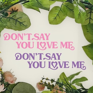 May include: A white background with green leaves surrounding the text "Don't Say You Love Me" in pink and purple lettering.