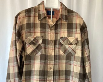 May include: A long-sleeve button-down shirt featuring a plaid pattern in shades of brown, tan, and cream with thin red accent lines. The shirt includes a standard collar, a front button placket, and two chest pockets with buttoned flaps.