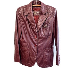 Pode incluir: Um blazer de couro bord&ocirc; com fecho de bot&atilde;o e dois bolsos. O blazer tem um pequeno bolso no peito esquerdo com um fecho de metal.