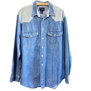 May include: A blue denim long-sleeve shirt with white and blue striped yoke panels. The shirt has a button-down collar, two chest pockets, and a single button cuff.