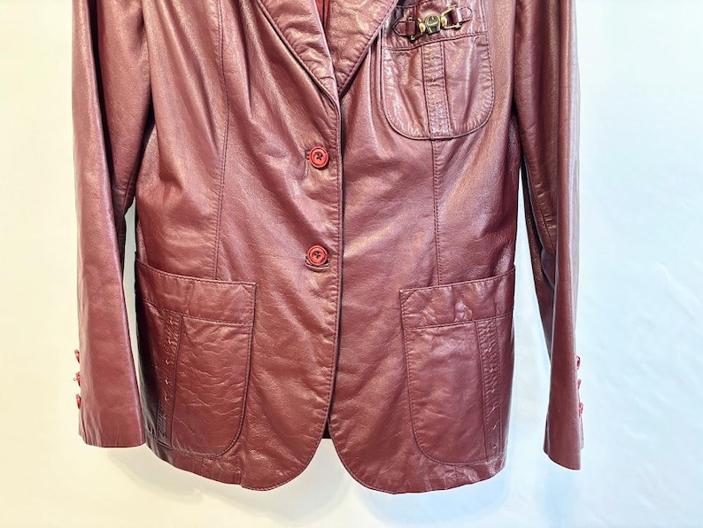 Pode incluir: Um blazer de couro bord&ocirc; com fecho de um s&oacute; bot&atilde;o e dois bolsos com aba. O blazer tem um detalhe met&aacute;lico decorativo no lado esquerdo do peito.