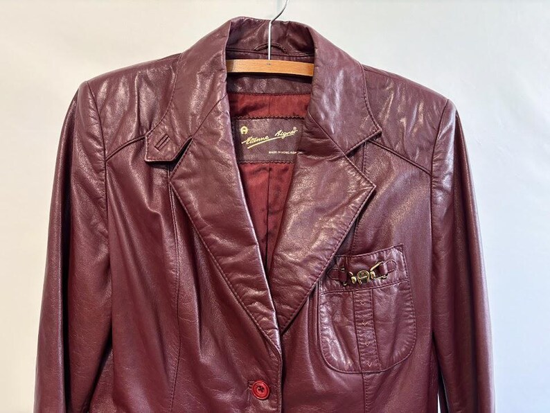 Pode incluir: Uma jaqueta de couro bord&ocirc; com um z&iacute;per dourado e uma etiqueta dourada que diz "Alma Regia" Feito em Hong Kong.