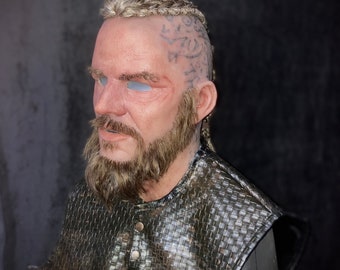 May include: A realistic-looking, detailed, brown and black,  silicone mask of a man with a braided beard and a braided hairstyle. The mask has a detailed, realistic face with a beard and a braided hairstyle. The mask is made of silicone and is designed to be worn over the face.