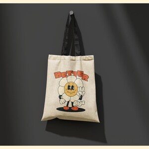 Pu&ograve; includere: Una borsa tote beige con manici neri. La borsa ha un fiore di cartone animato con un viso sorridente e le parole "Better Days" stampate su di essa.