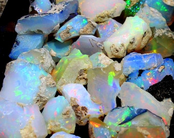 May include: A collection of rough, natural opal gemstones in various shades of white, blue, and green. The opals have an iridescent sheen and are displayed on a black surface.