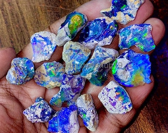 May include: A collection of rough, uncut opals in various shapes and sizes. The opals display vibrant colors, including blues, greens, and flashes of iridescent hues. The stones are held in a hand, showcasing their natural, raw beauty.