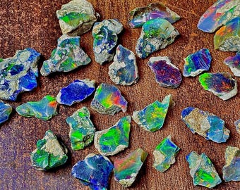 May include: A collection of raw opal gemstones, displaying a vibrant array of colors including blues, greens, and flashes of rainbow hues. The opals are rough-cut, showcasing their natural, unpolished state. The gemstones are scattered on a wooden surface.