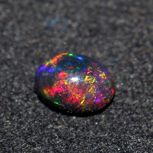 Puede incluir: Una piedra preciosa de ópalo negro con un arcoíris de colores, incluyendo rojo, naranja, amarillo, verde, azul y morado.