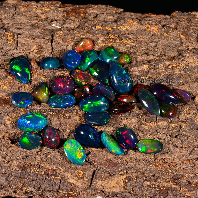 May include: A collection of black opal gemstones in various shapes and sizes, with iridescent colors of green, blue, red, and purple. The gemstones are displayed on a piece of rough-hewn wood.
